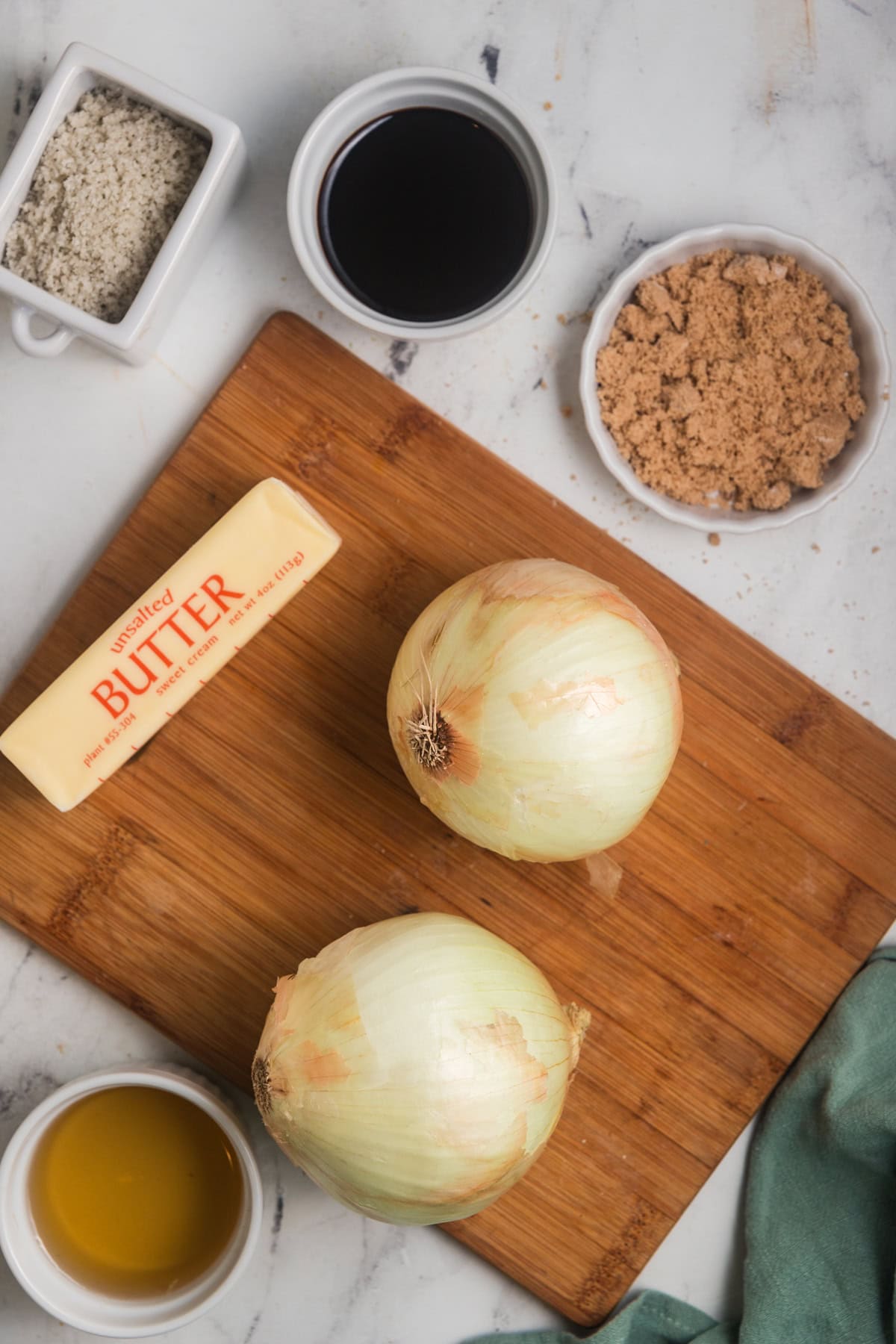 Ingredients needed to make homemade onion jam laid out on a wooden cutting board. 