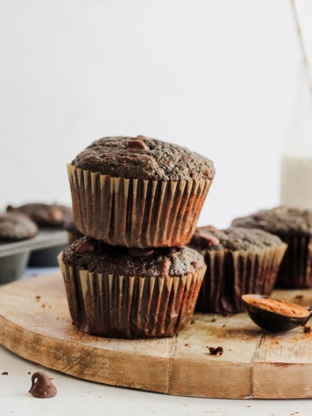 stacked chocolate muffins on a wooden board, with milk in the background.