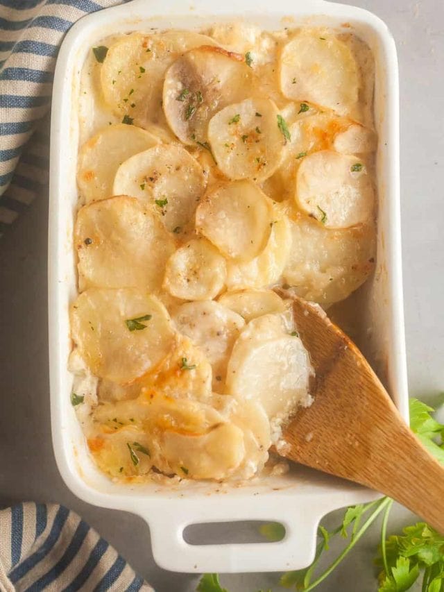 Taking a scoop out of a pan of cheesy scalloped potatoes.