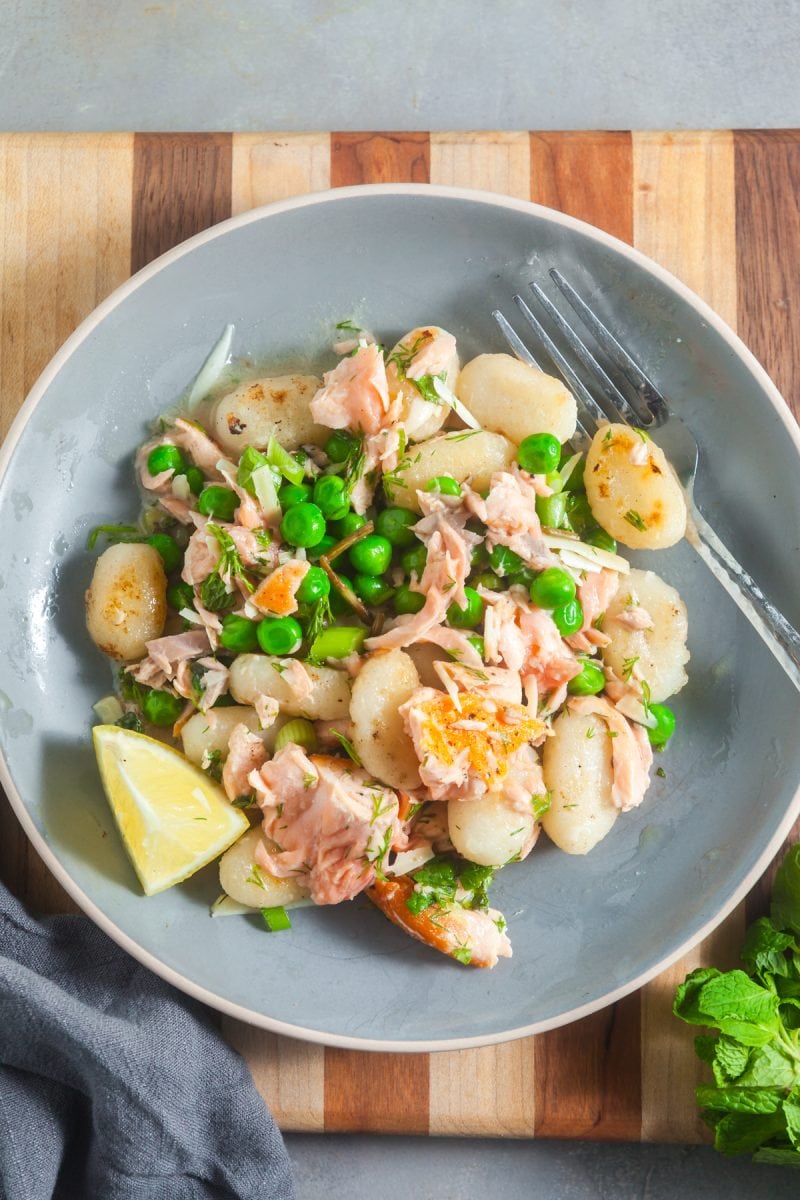 Overhead view of a plate of gnocchi with salmon, peas, and fresh herbs. 