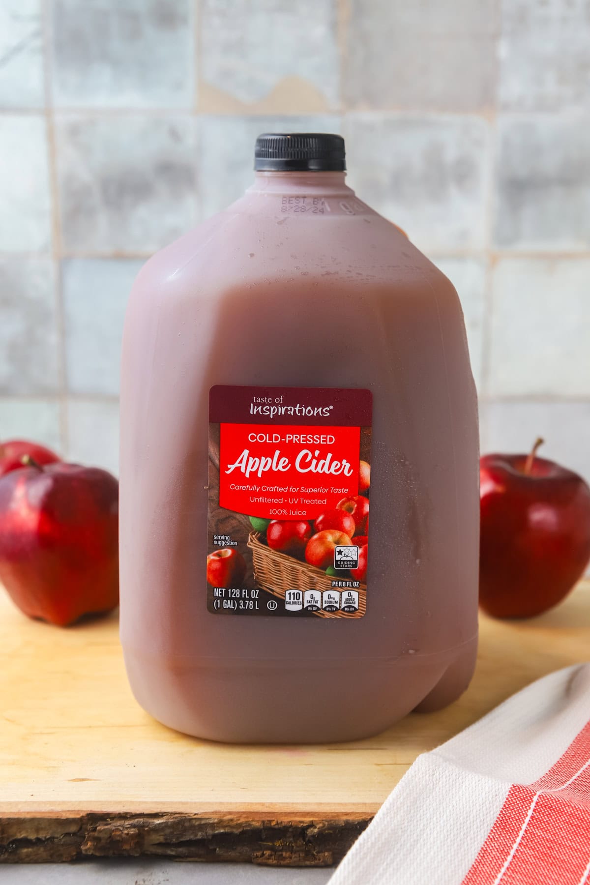 A gallon of apple cider on a wooden cutting board. There are apples in the background. 