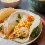 A speckled plate of two tacos filled with sautéed shrimp and Mexican-inspired street corn.