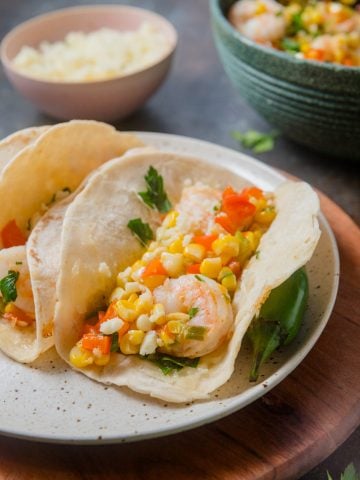 A speckled plate of two tacos filled with sautéed shrimp and Mexican-inspired street corn.