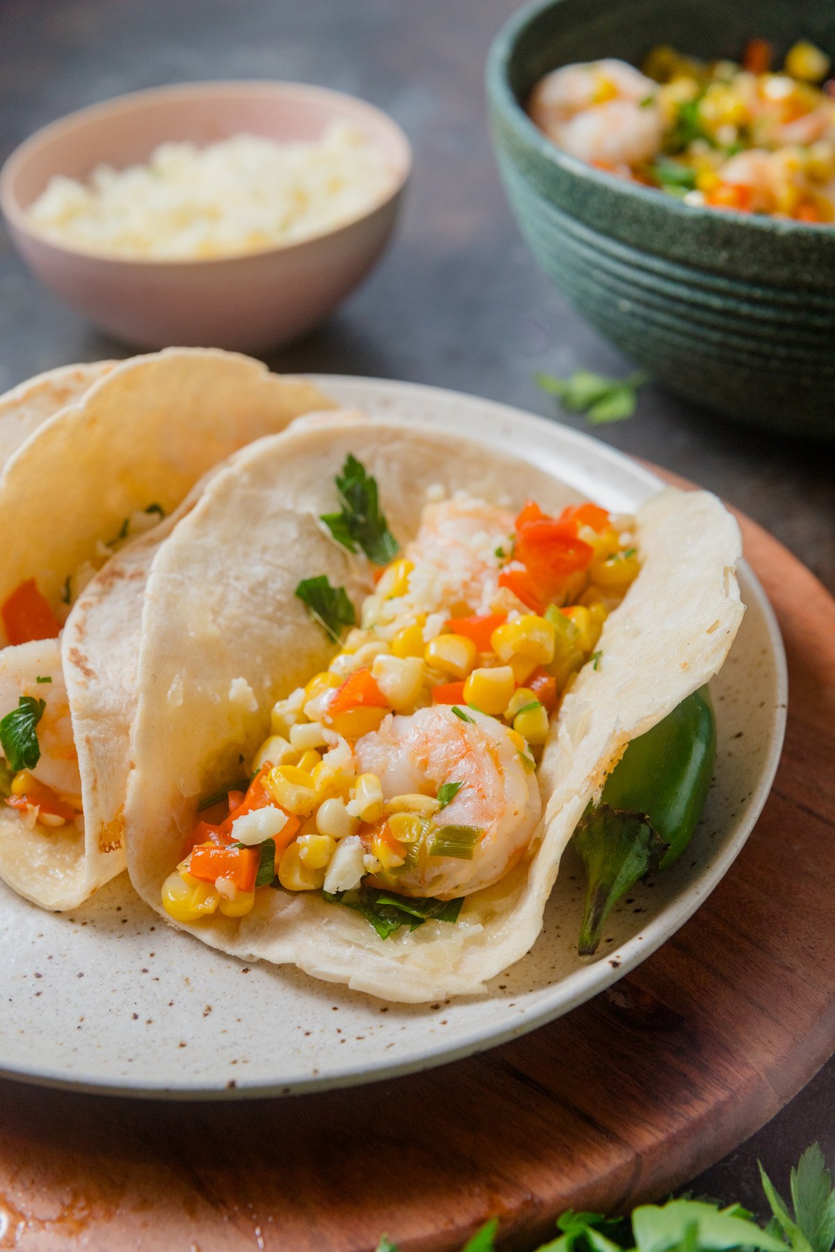 A speckled plate of two tacos filled with sautéed shrimp and Mexican-inspired street corn.