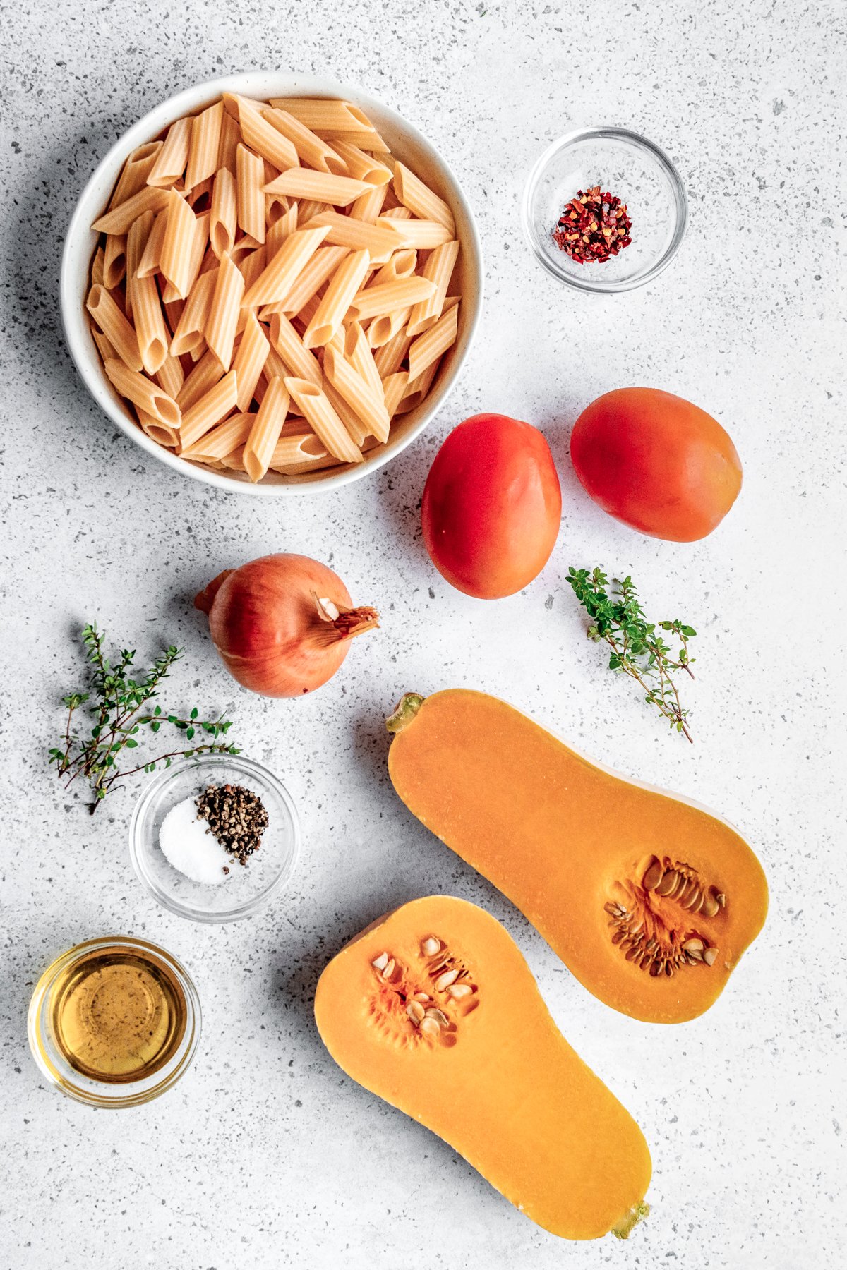 An overhead view of the ingredients needed to make butternut squash pasta, including squash, tomatoes, onion, and fresh thyme. 