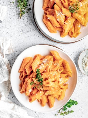 Two plate of penne pasta in butternut squash pasta sauce on a white speckled background.