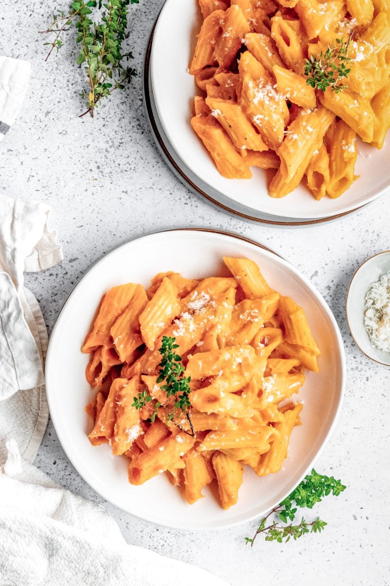 Two plate of penne pasta in butternut squash pasta sauce on a white speckled background.