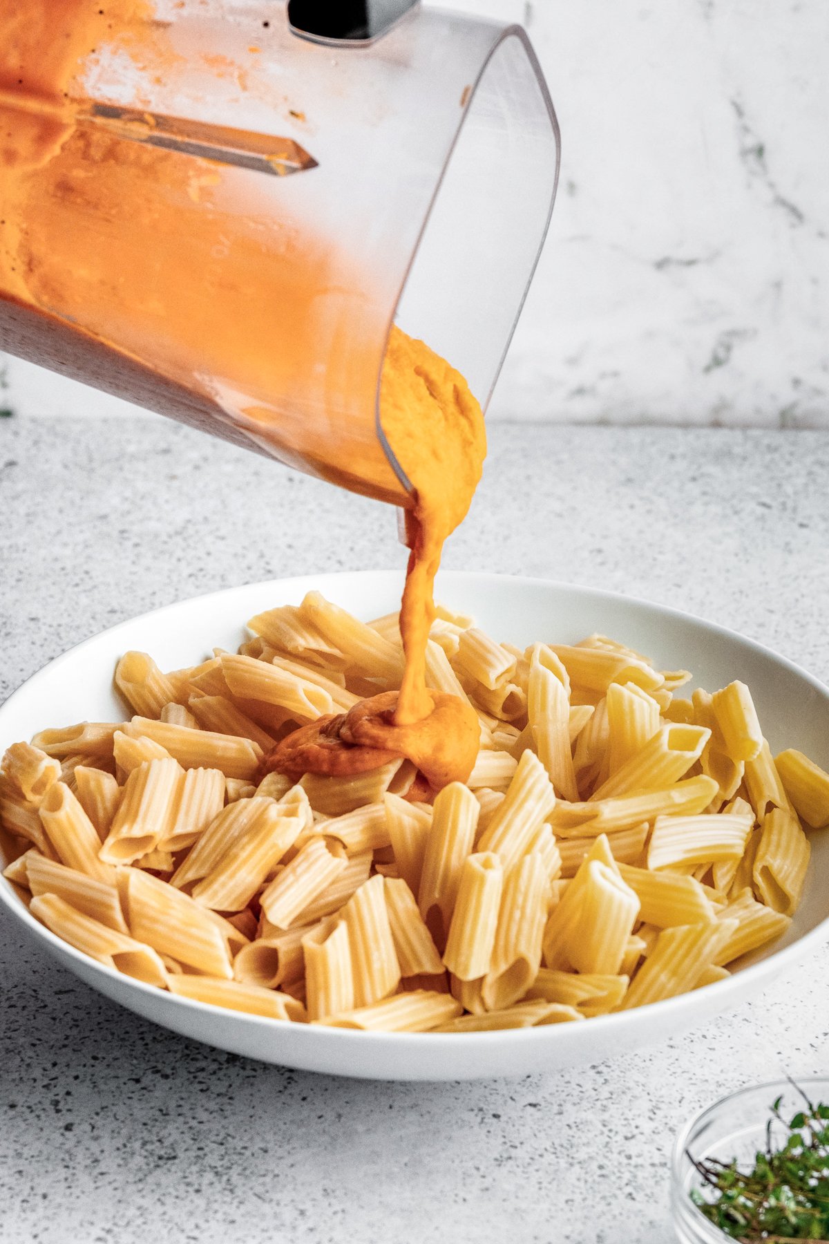 Pouring the butternut squash sauce onto cooked pasta.