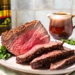 Medium-rare air fryer roast beef on a white platter with wine and gravy in the background.