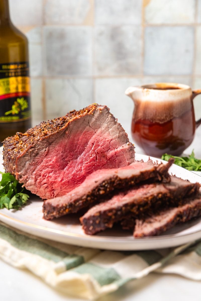 Medium-rare air fryer roast beef on a white platter with wine and gravy in the background. 